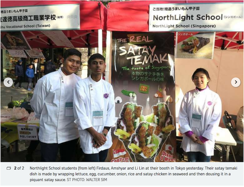Three NorthLight School Singapore students in white chef uniforms stand at a satay temaki food booth in Tokyo.
